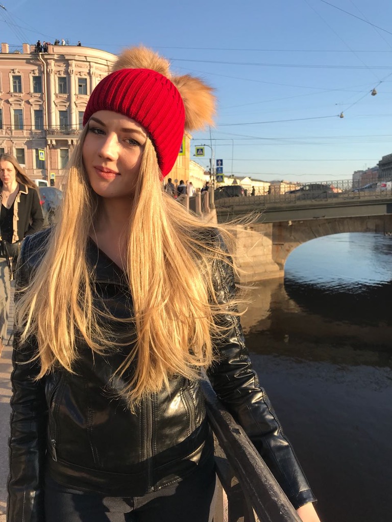 woman wearing red beanie with two gold fox fur pom-poms and brim